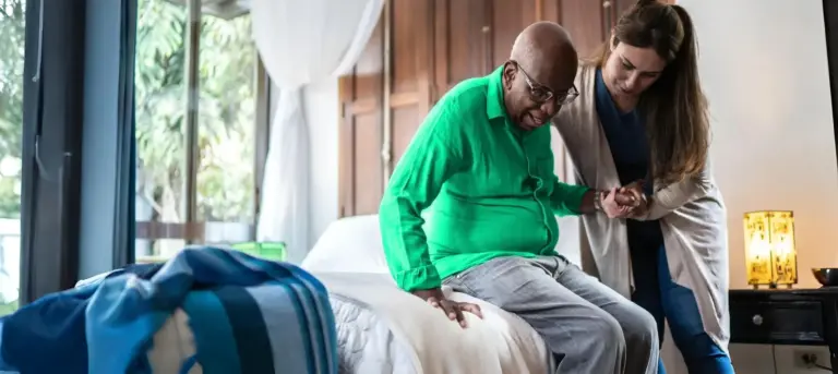 A care worker helping an older man out of bed at home