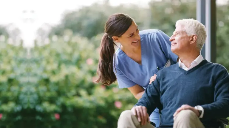A care worker smiling with an older man beside a garden window