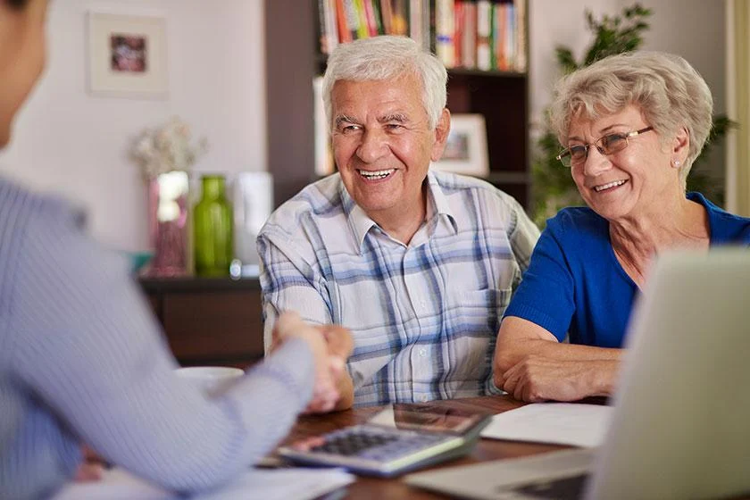 A retired couple shaking hands with their advisor across a desk.
