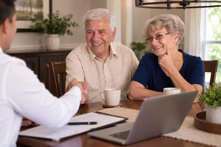 A retired couple shaking hands with their advisor across a dining table.